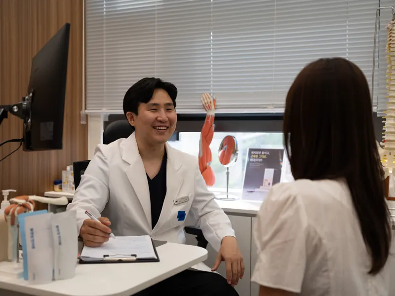 몸앤장한의원 진료실에서 원장이 환자와 웃으며 상담하는 모습